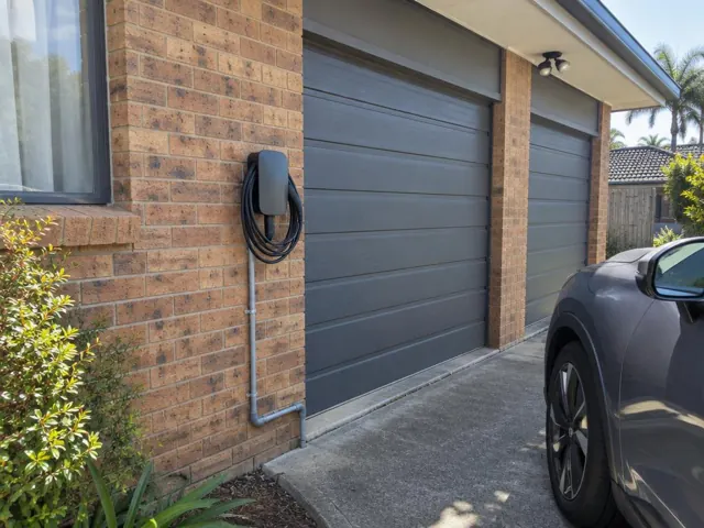 EV charger mounted on a brick garage wall beside a driveway in Thornton
