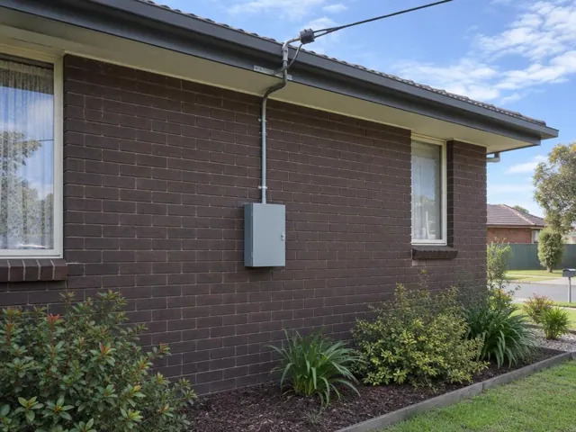 Brick house exterior with overhead service cable and point-of-attachment bracket above a meter box in Chisholm